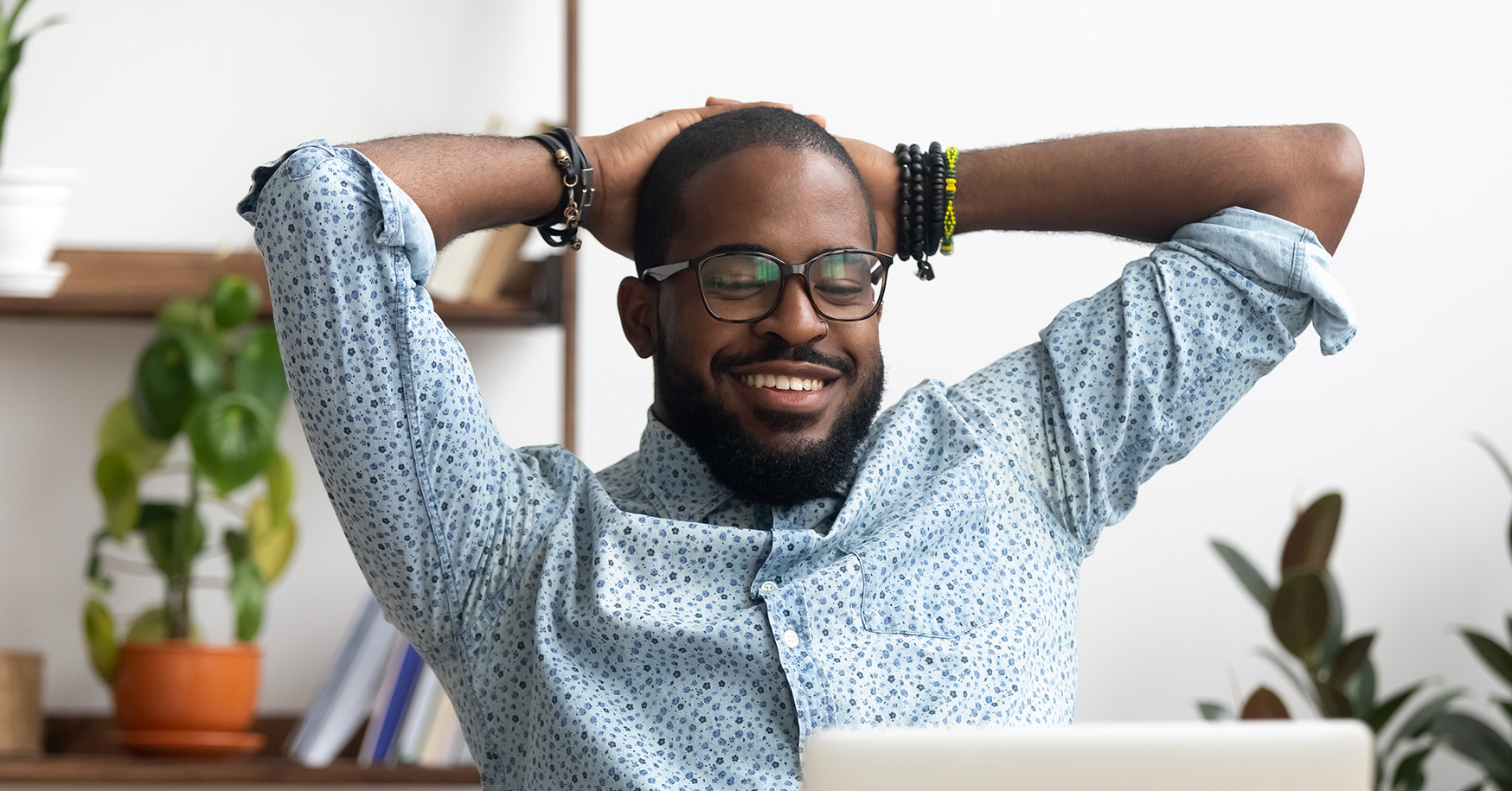 Man with hands behind head relaxed looking at laptop