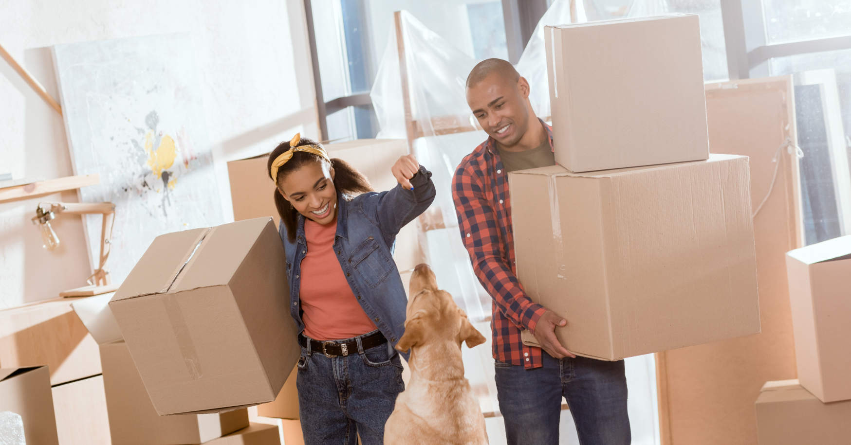 Man and woman carrying boxes into new home playing with dog